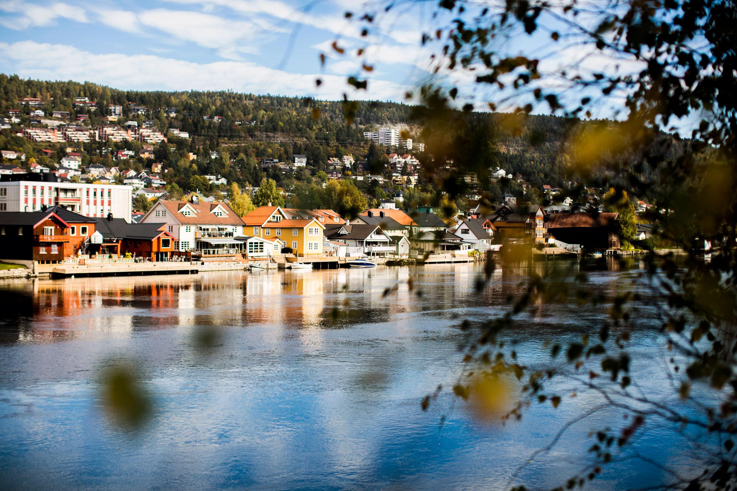 Koselig husbebygning bak trærne og over elven. Nye leiligheter i Elvekvartalet
